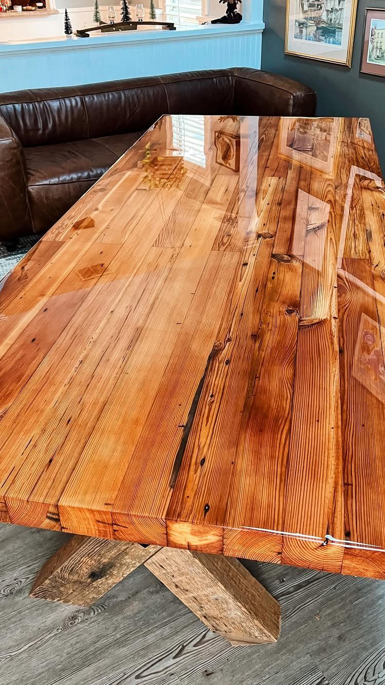 Reclaimed wood dining table with a glossy finish and heavy X-shaped wooden base.