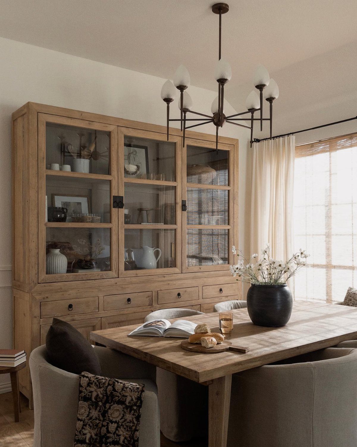 Wooden dining table and large glass-door hutch in a bright, neutral room.