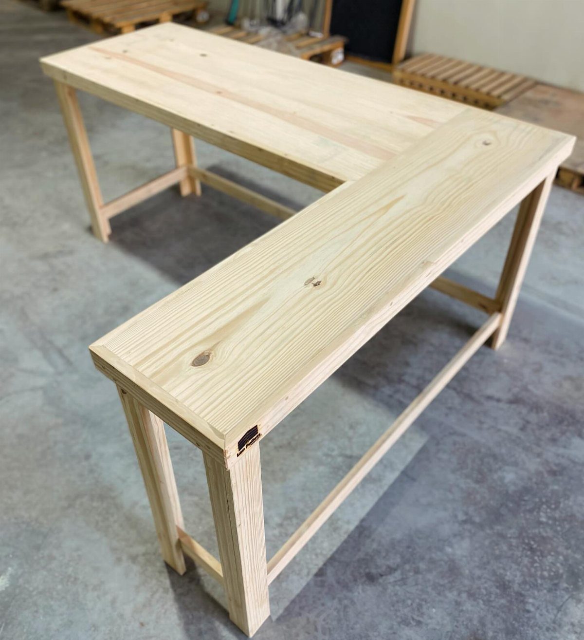 L-shaped desk made of light natural wood on a grey concrete floor.