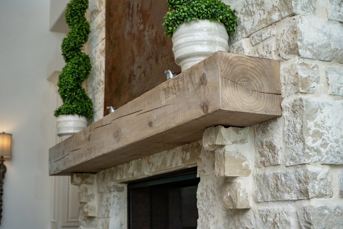Rustic reclaimed wood beam mantel mounted on a light stone fireplace wall