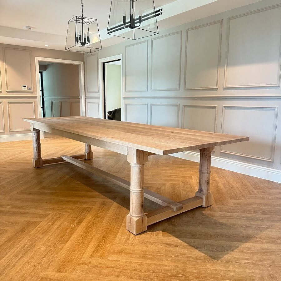 Long reclaimed wood dining table with trestle base on herringbone wood flooring.