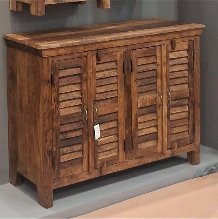 Rustic reclaimed wood sideboard with shutter-style doors and metal handles against grey wall.