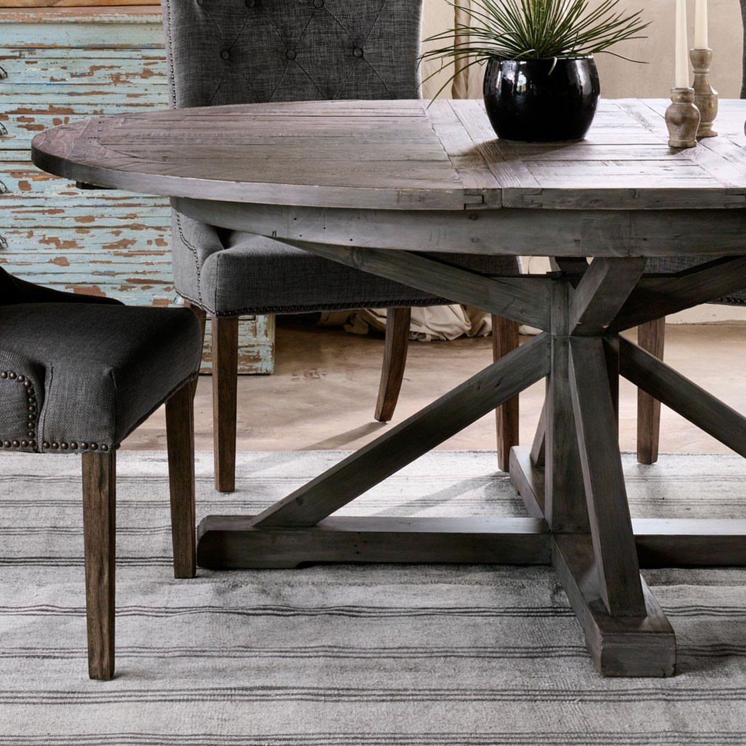 Round reclaimed wood dining table with X-shaped base and grey upholstered chairs.