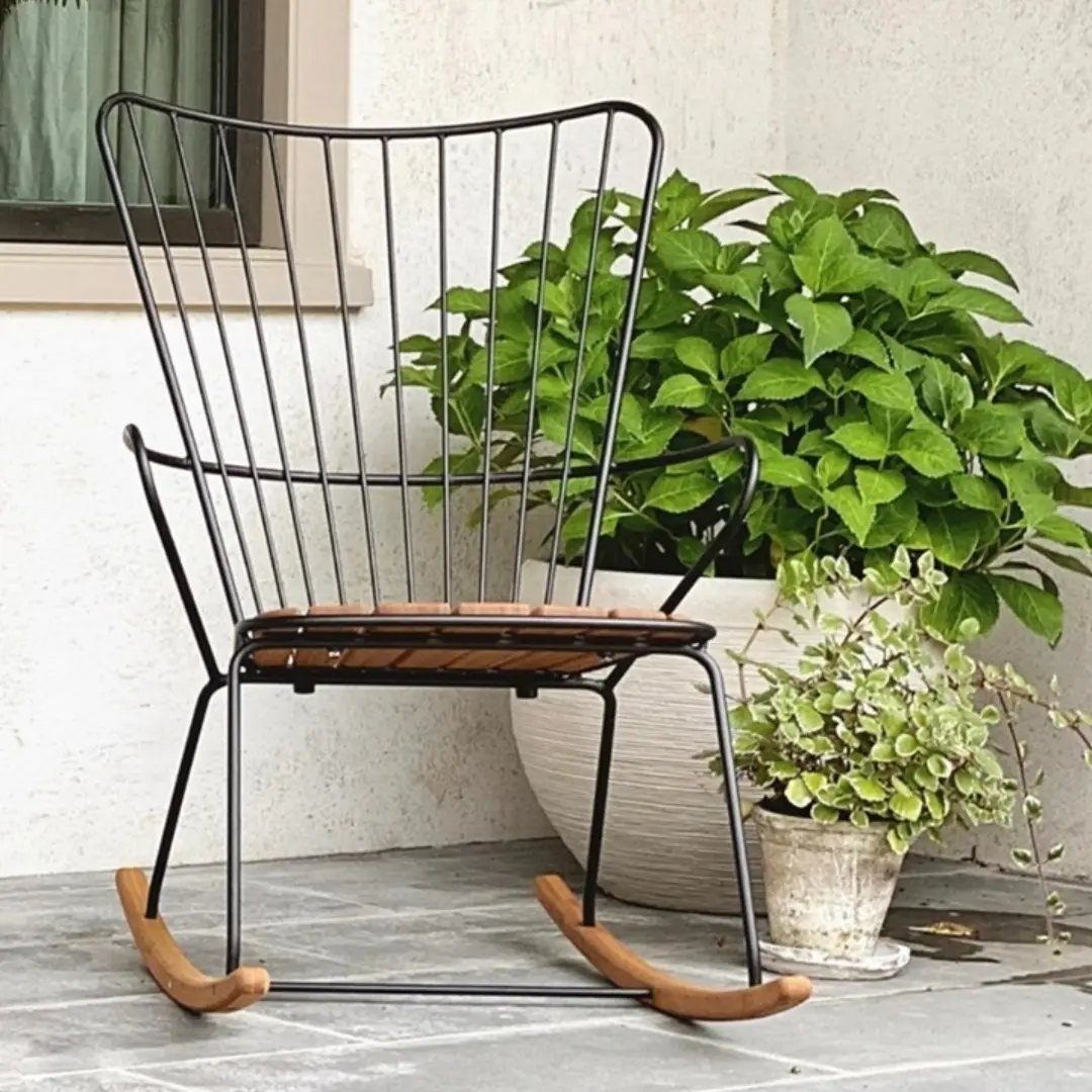 29 Scandinavian Outdoor Furniture for Patios and Gardens 6 Black metal rocking chair with wooden seat on a stone patio with plants.