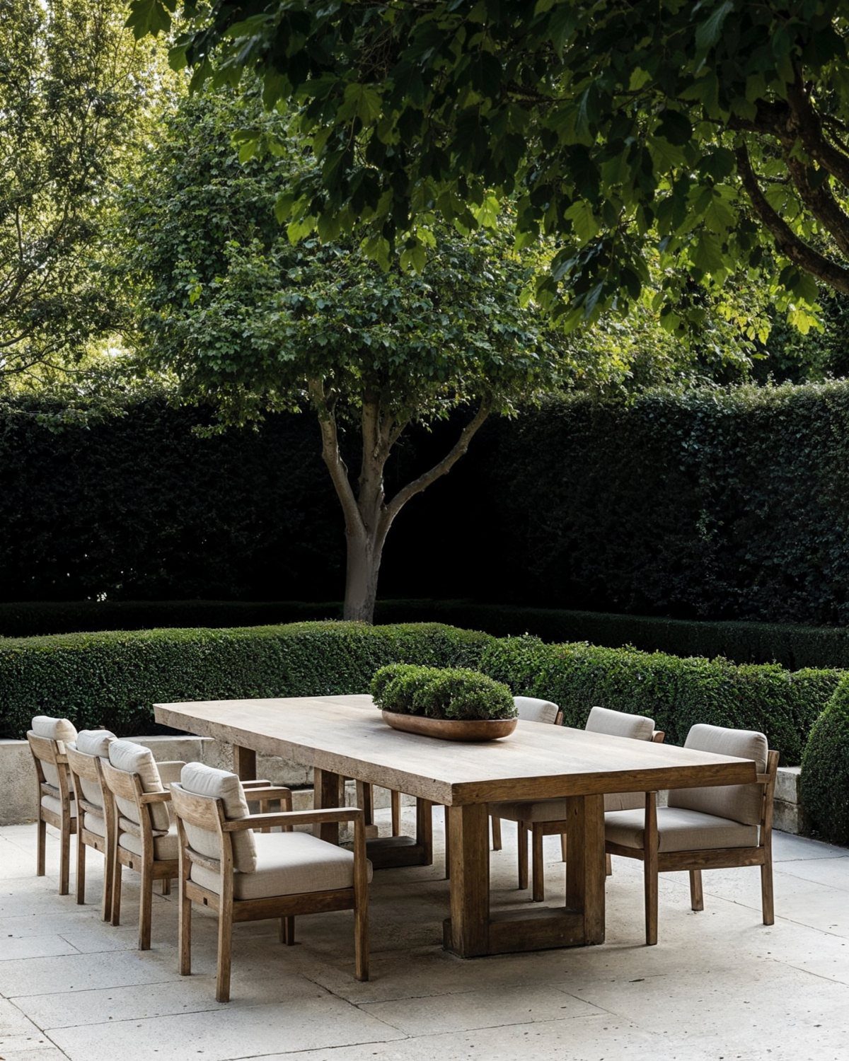 29 Scandinavian Outdoor Furniture for Patios and Gardens 3 Wooden outdoor dining table and chairs on a stone patio with green hedges.