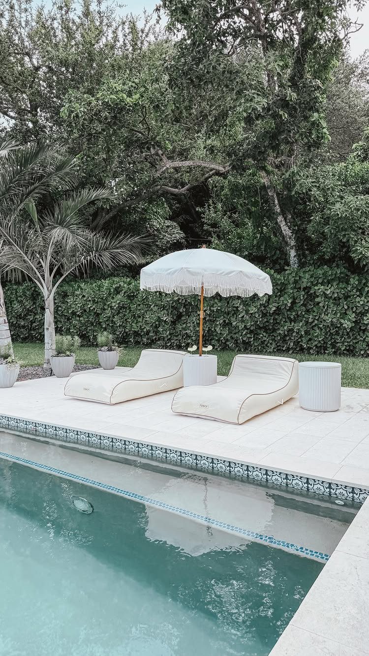 29 Scandinavian Outdoor Furniture for Patios and Gardens 12 White sun loungers and a small cylindrical side table by a swimming pool.
