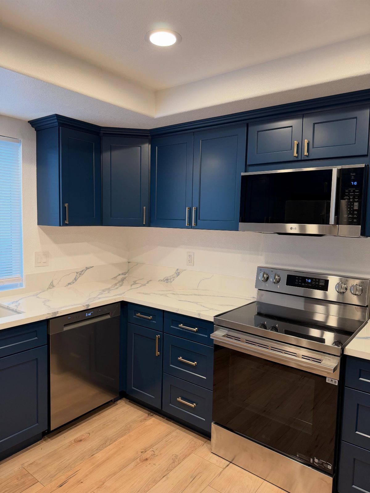 Navy blue shaker cabinets in a U-shaped kitchen with white marble countertops.