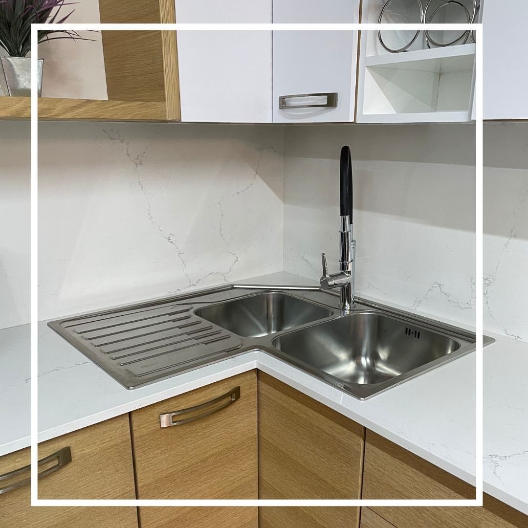 Diagonal stainless steel double sink installed in a white marble kitchen corner countertop.