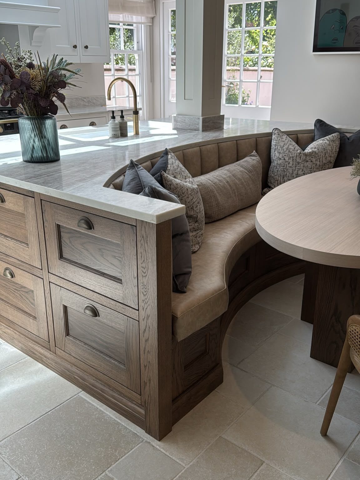 Curved wooden kitchen peninsula with white countertop and built-in banquette seating area.