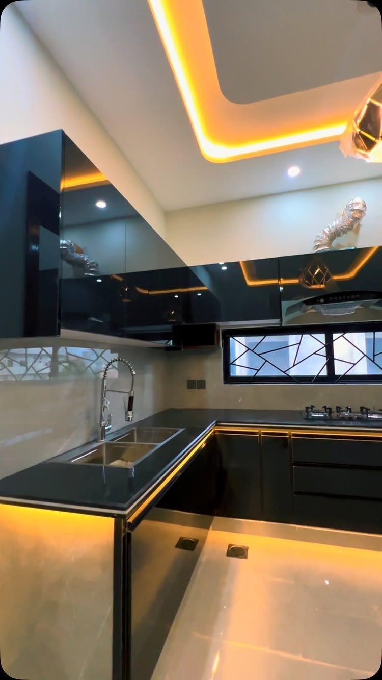 Modern U-shaped kitchen with dark glossy cabinets and warm yellow recessed lighting.