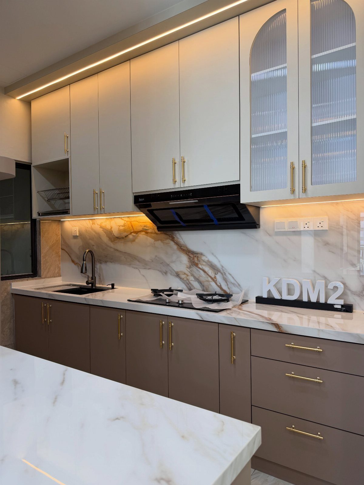 Modern kitchen with sleek slab doors in off-white and taupe with gold handles.