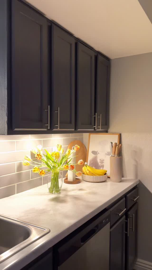 Dark grey kitchen cabinets with under-cabinet lighting illuminating yellow tulips on a white countertop.