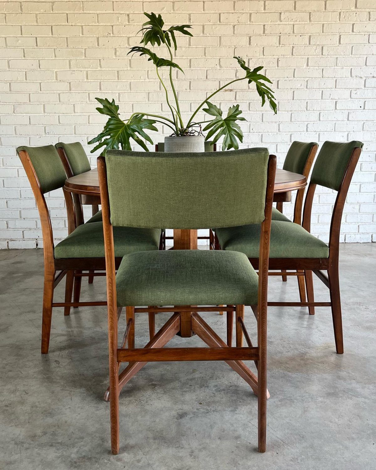 Solid Wood Dining Table Set: 20 Ideas for Your Home 13 Mid-century modern round wooden dining table with green upholstered chairs against white brick wall.