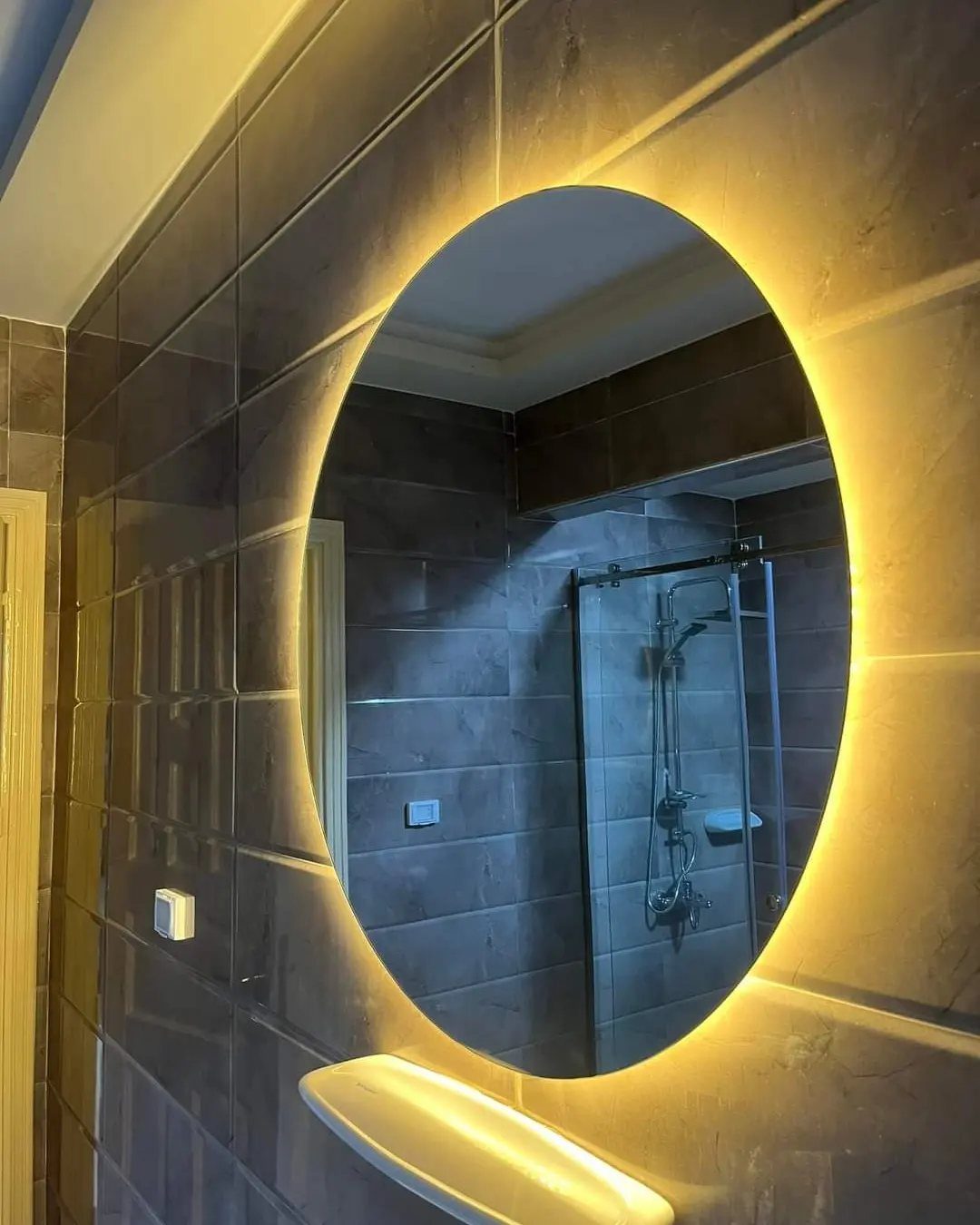 19 Teen Bathroom Ideas That Blend Style and Function 8 Round backlit mirror with glowing yellow light on a dark tiled bathroom wall