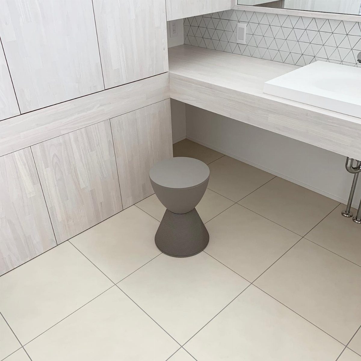 19 Teen Bathroom Ideas That Blend Style and Function 14 Grey hourglass stool tucked under a white floating bathroom vanity with wood paneling.