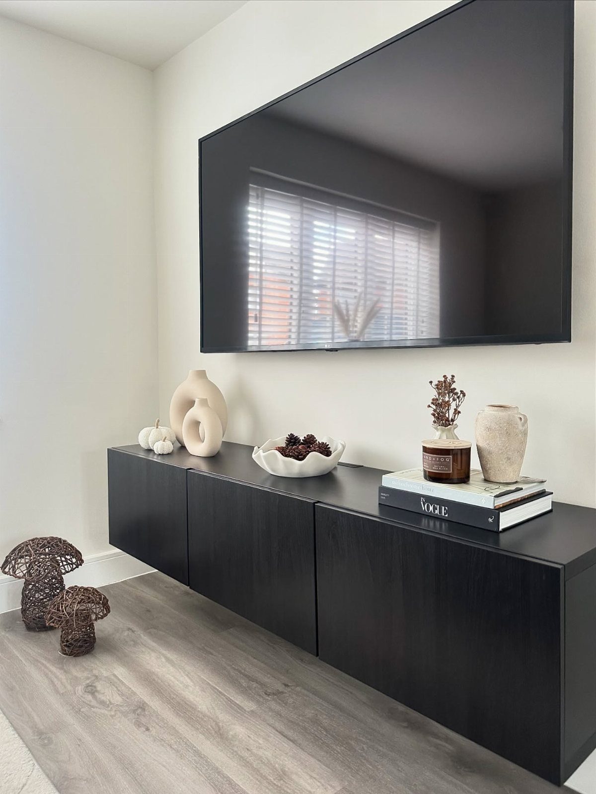 Black media console with decorative vases and books beneath a wall-mounted television.