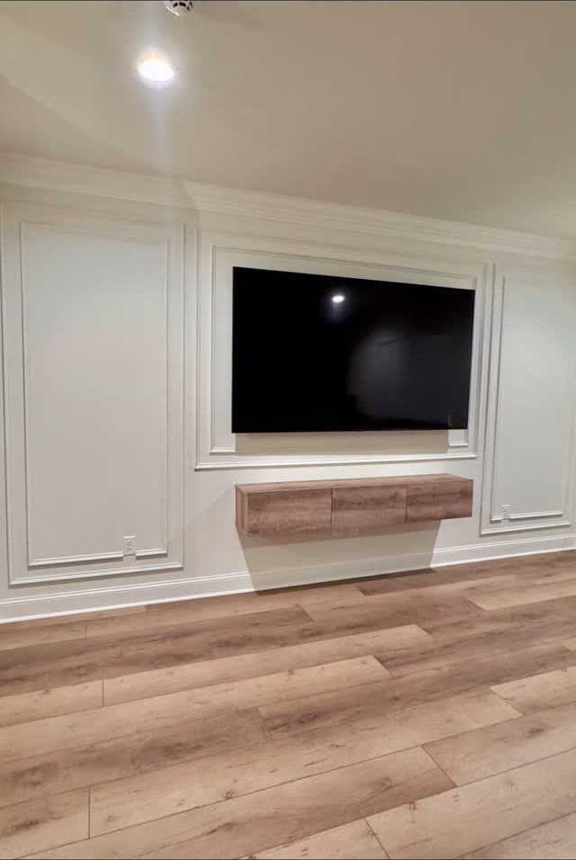 White picture frame molding on a wall with a mounted TV and floating console.
