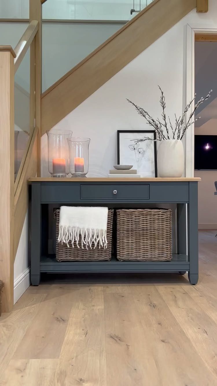 Dark grey console table with woven baskets on the lower shelf under a staircase.
