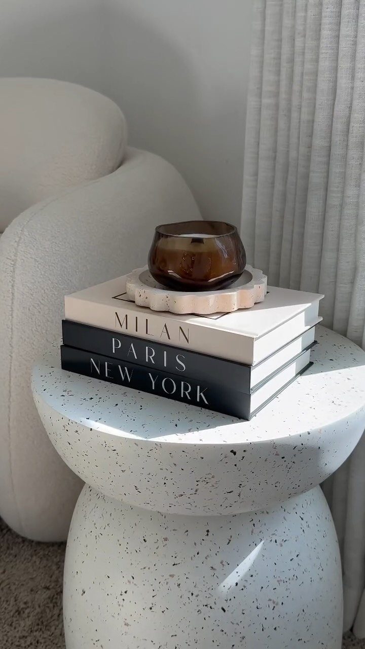 Stacked books with a candle on a white speckled stone pedestal table.