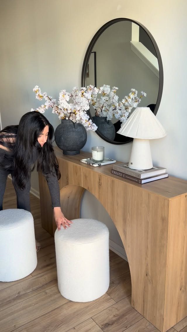 Round black-framed mirror hanging above a light wood console table with white decor.