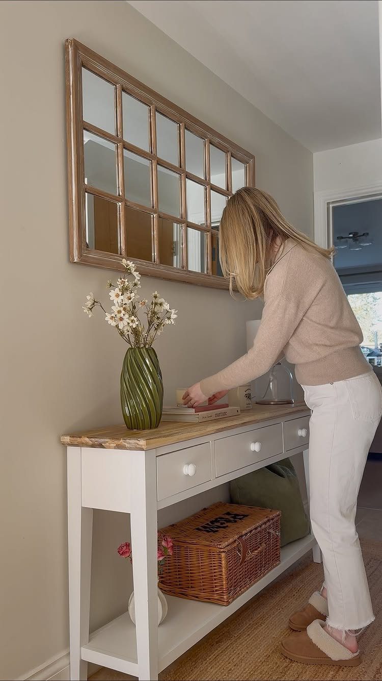 Narrow white console table with a windowpane mirror and wicker basket in a hallway.