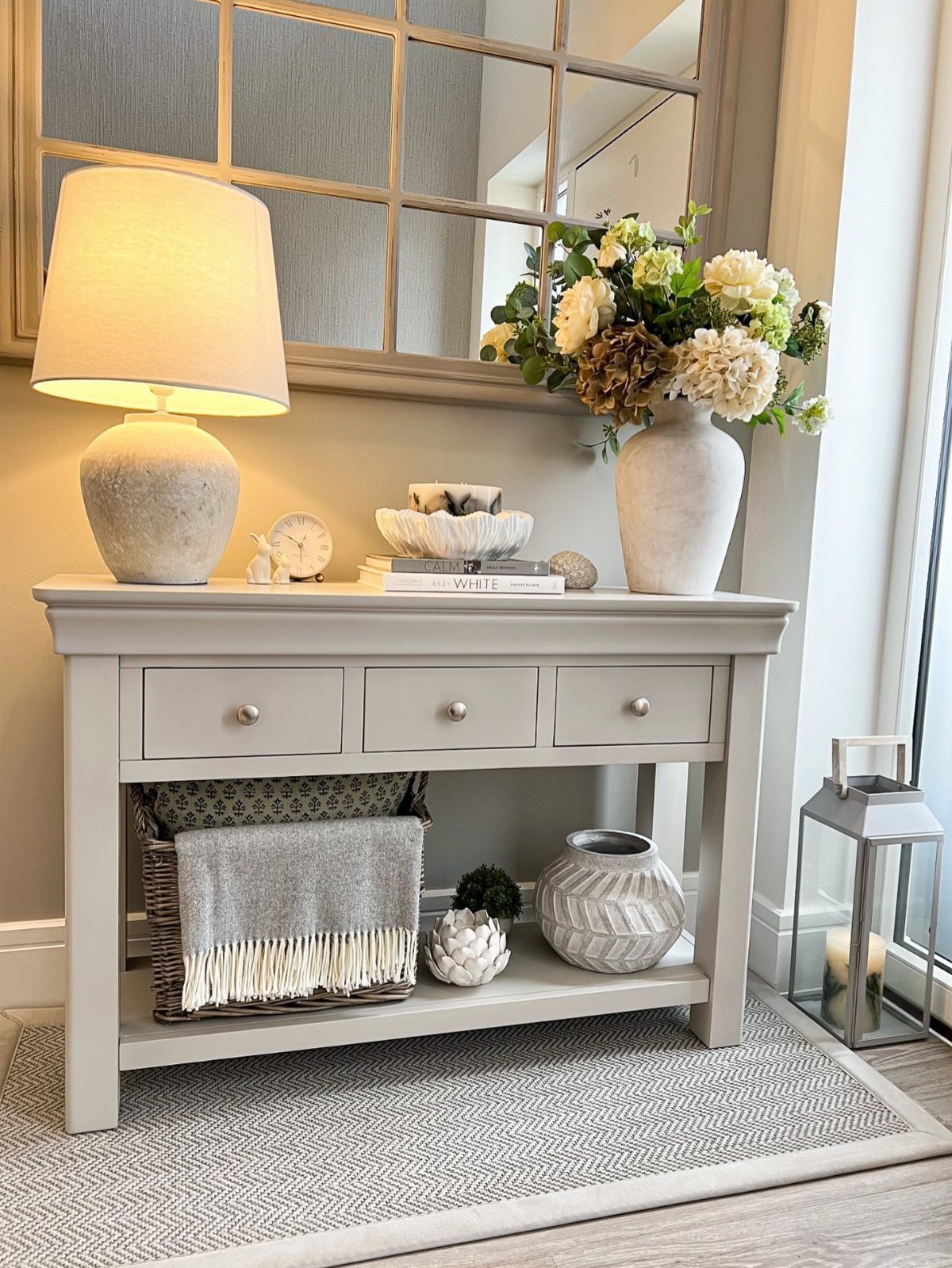 Console table with a gray fringed throw blanket in a basket on the lower shelf.