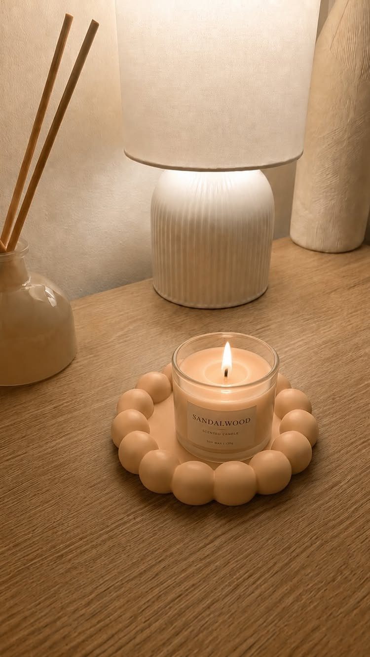Lit candle on a bubble tray next to a white ribbed table lamp.