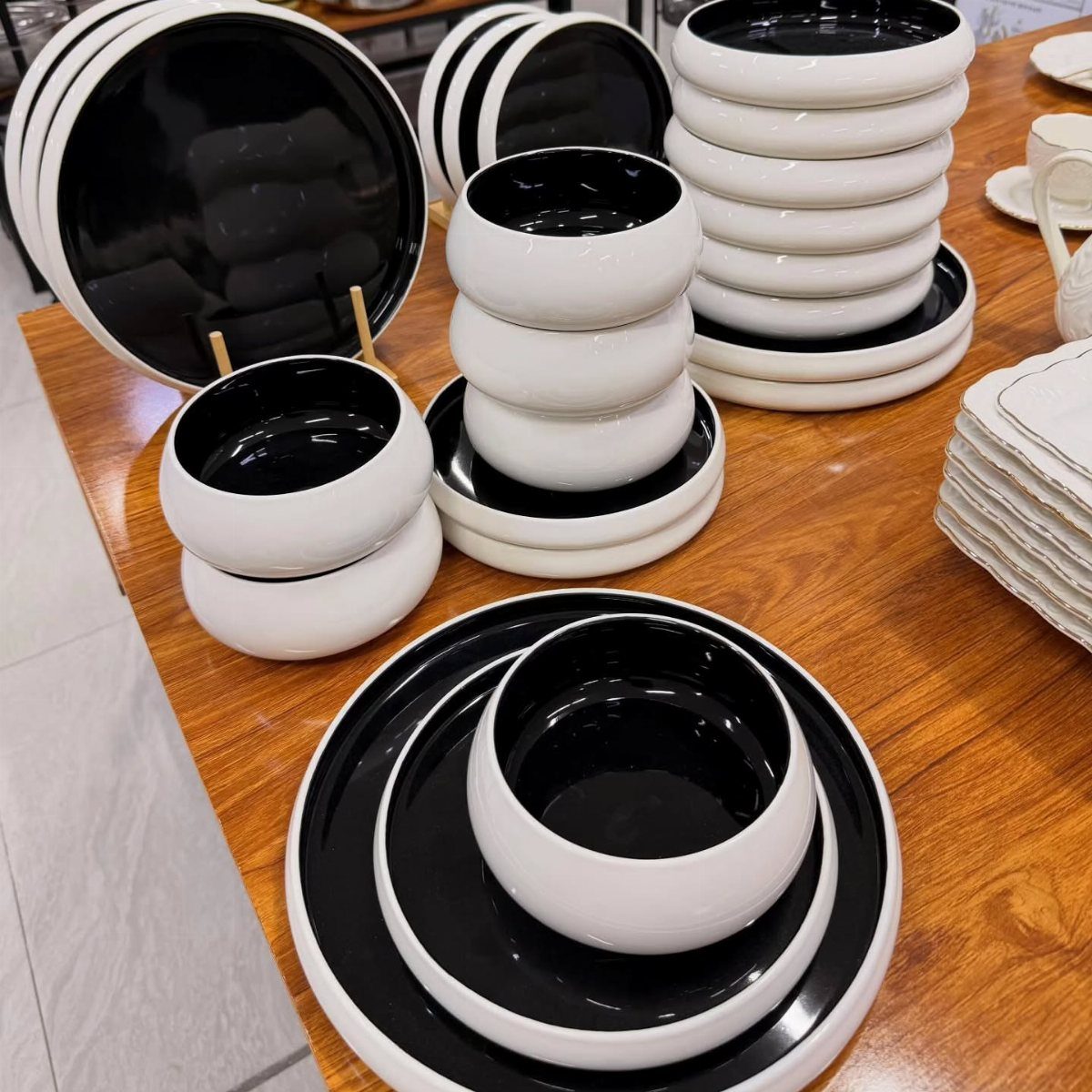 White stoneware dishes with black interiors arranged on a polished wooden table.