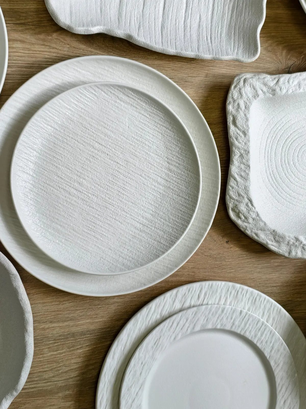 White rimless coupe plates and organic stoneware platters on a light wooden table