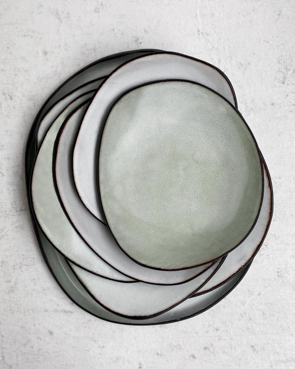 Stacked off-white ceramic plates with irregular organic shapes and dark brown rims.