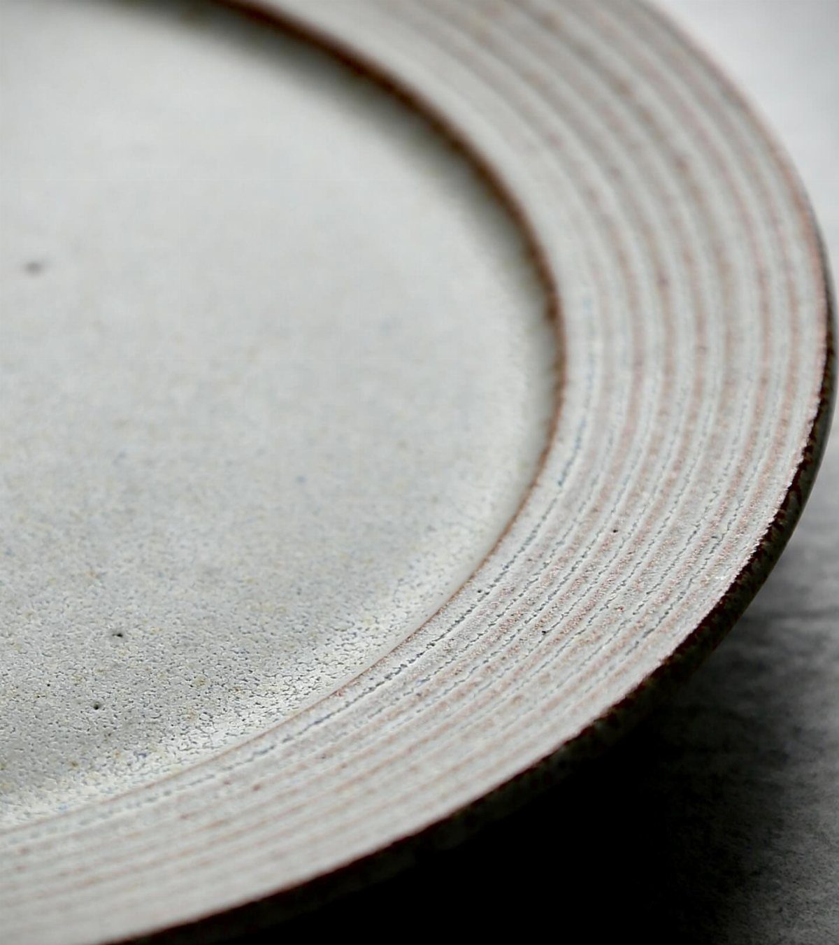 White stoneware plate with a matte finish and ribbed concentric rings on the rim.