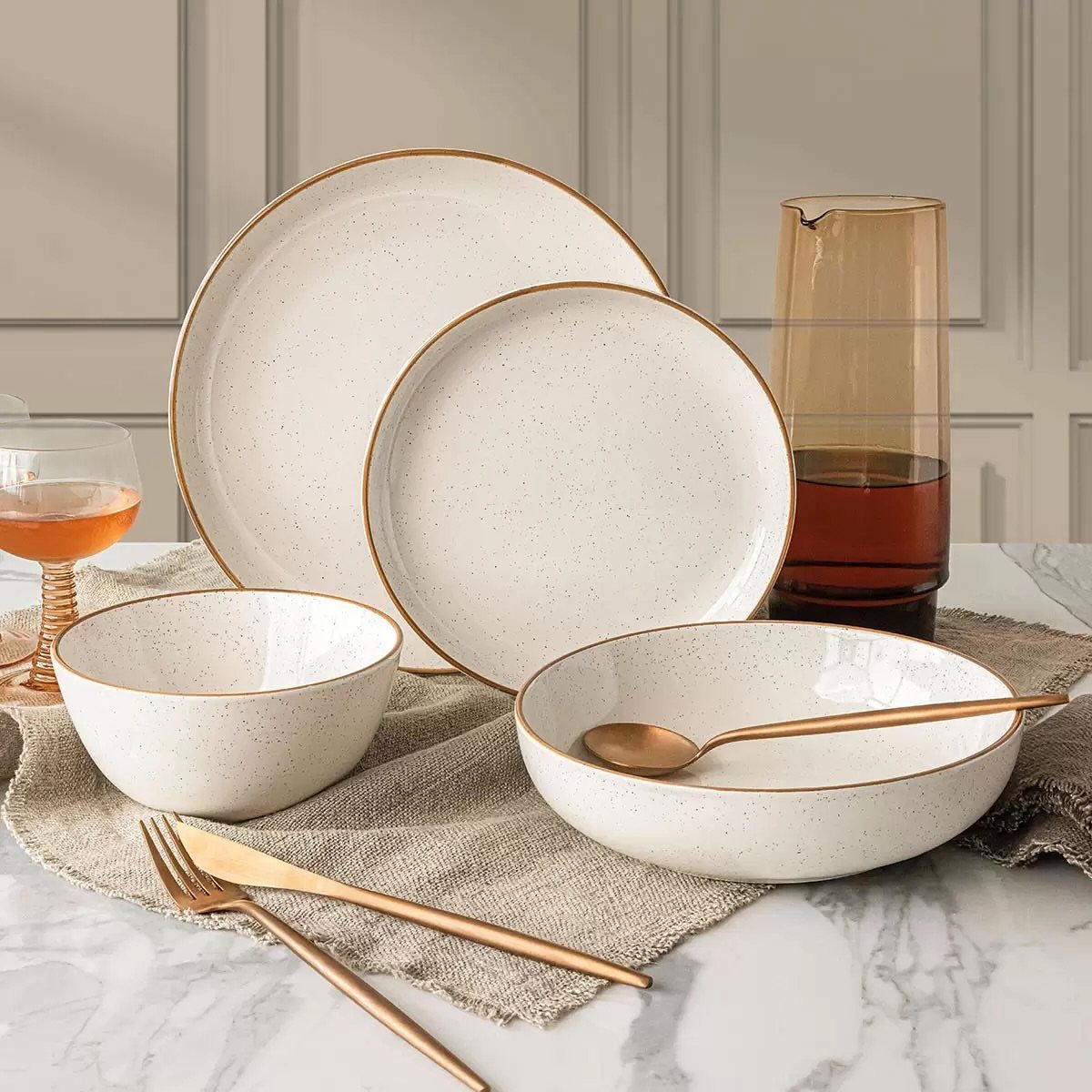 White speckled stoneware plates and bowls with gold rims on a marble table.