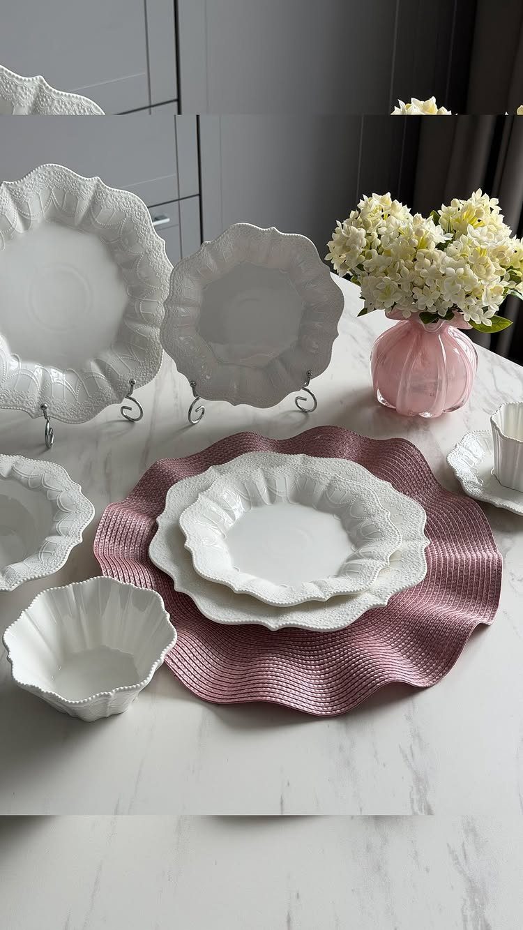 White stoneware dishes with ruffled edges on a marble table with pink accents.