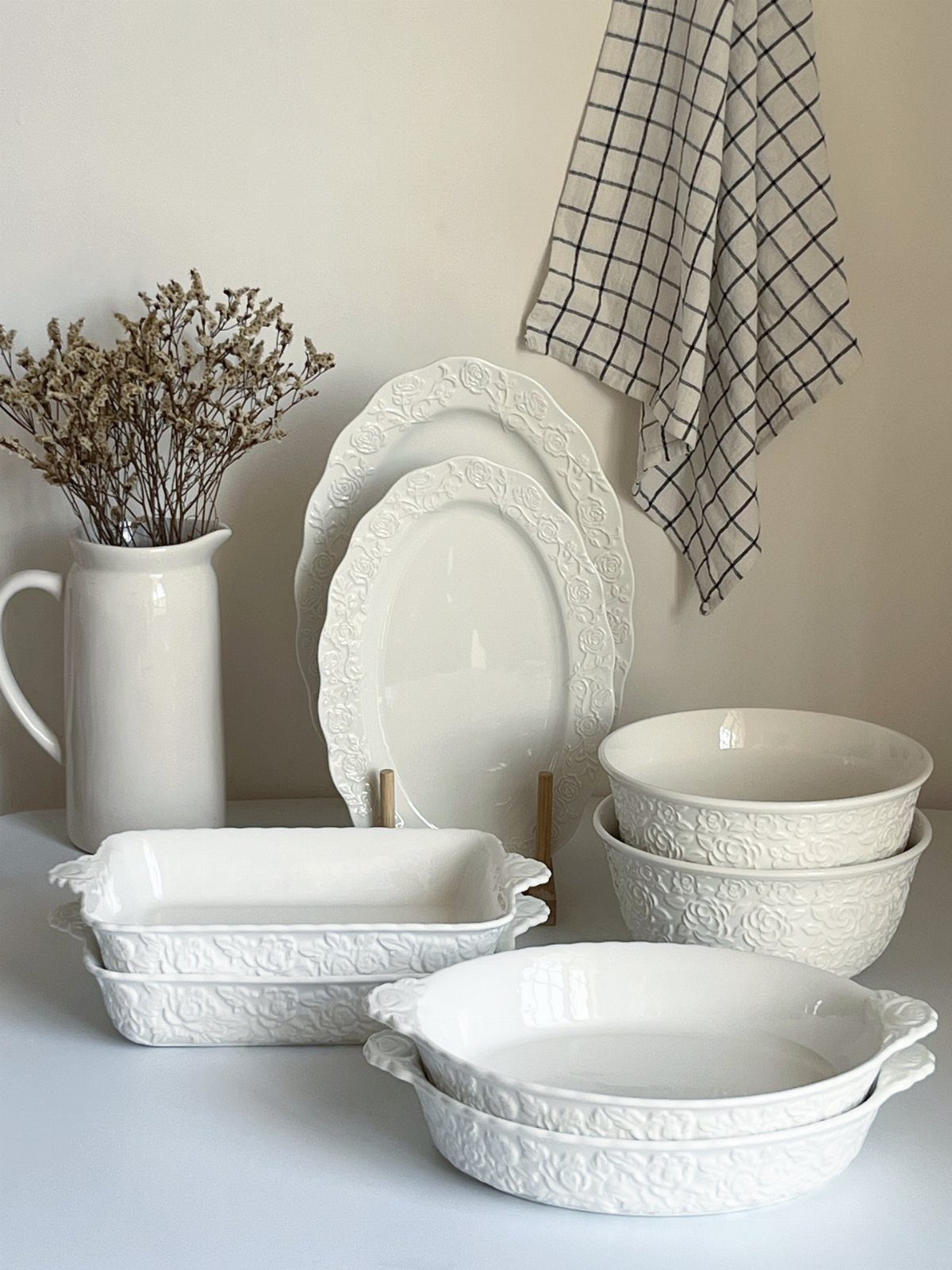 White stoneware serving pieces with embossed floral patterns and scalloped edges on a table.