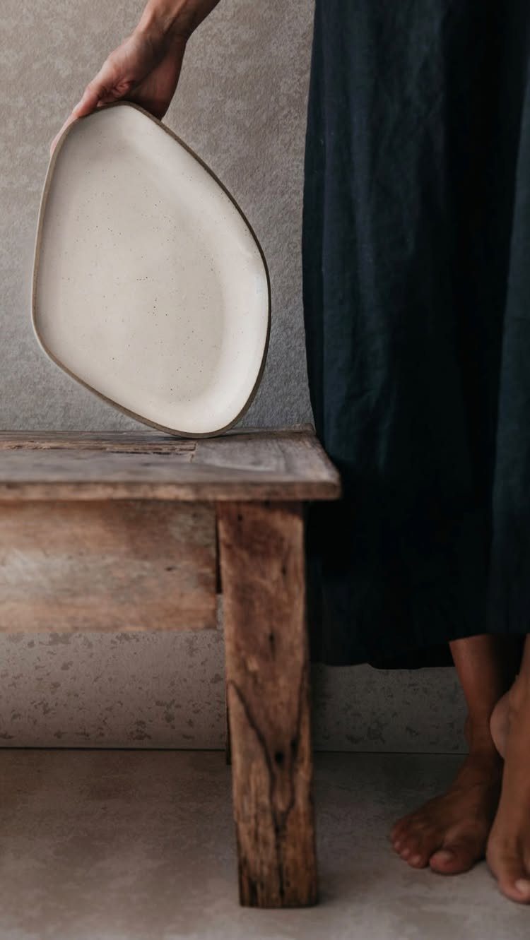 Off-white speckled stoneware plate held by a person over a rustic wooden stool.