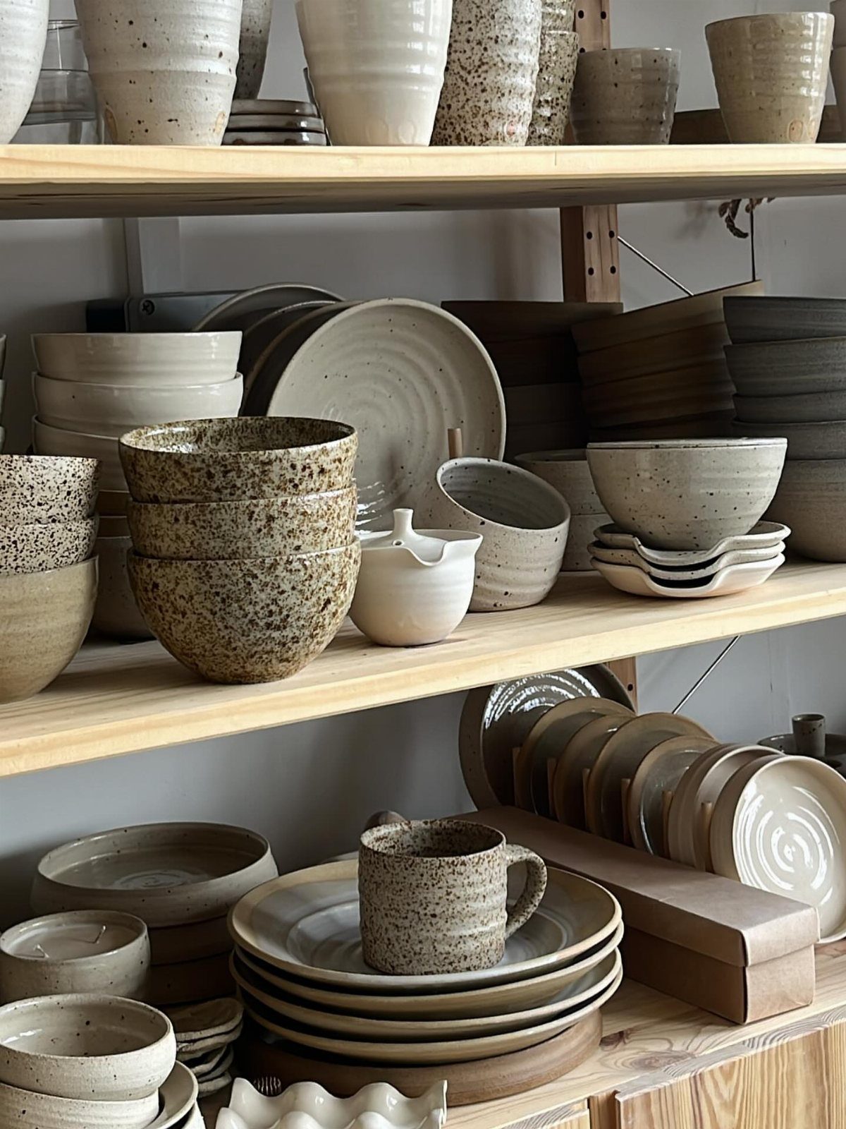 Speckled white stoneware bowls and plates displayed on light wooden open shelving.