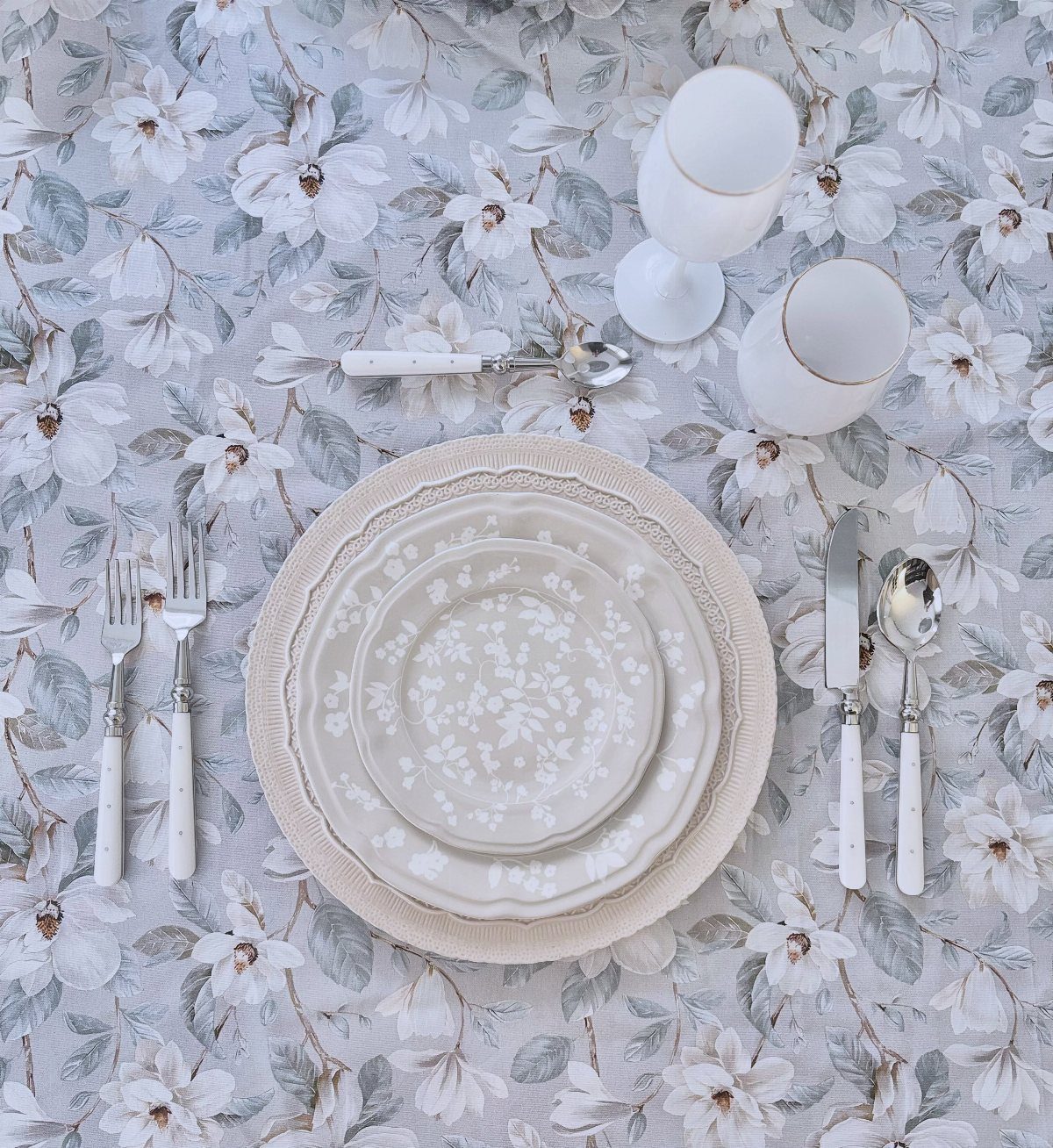 White dinnerware set with floral plates on a matching floral tablecloth and linens.