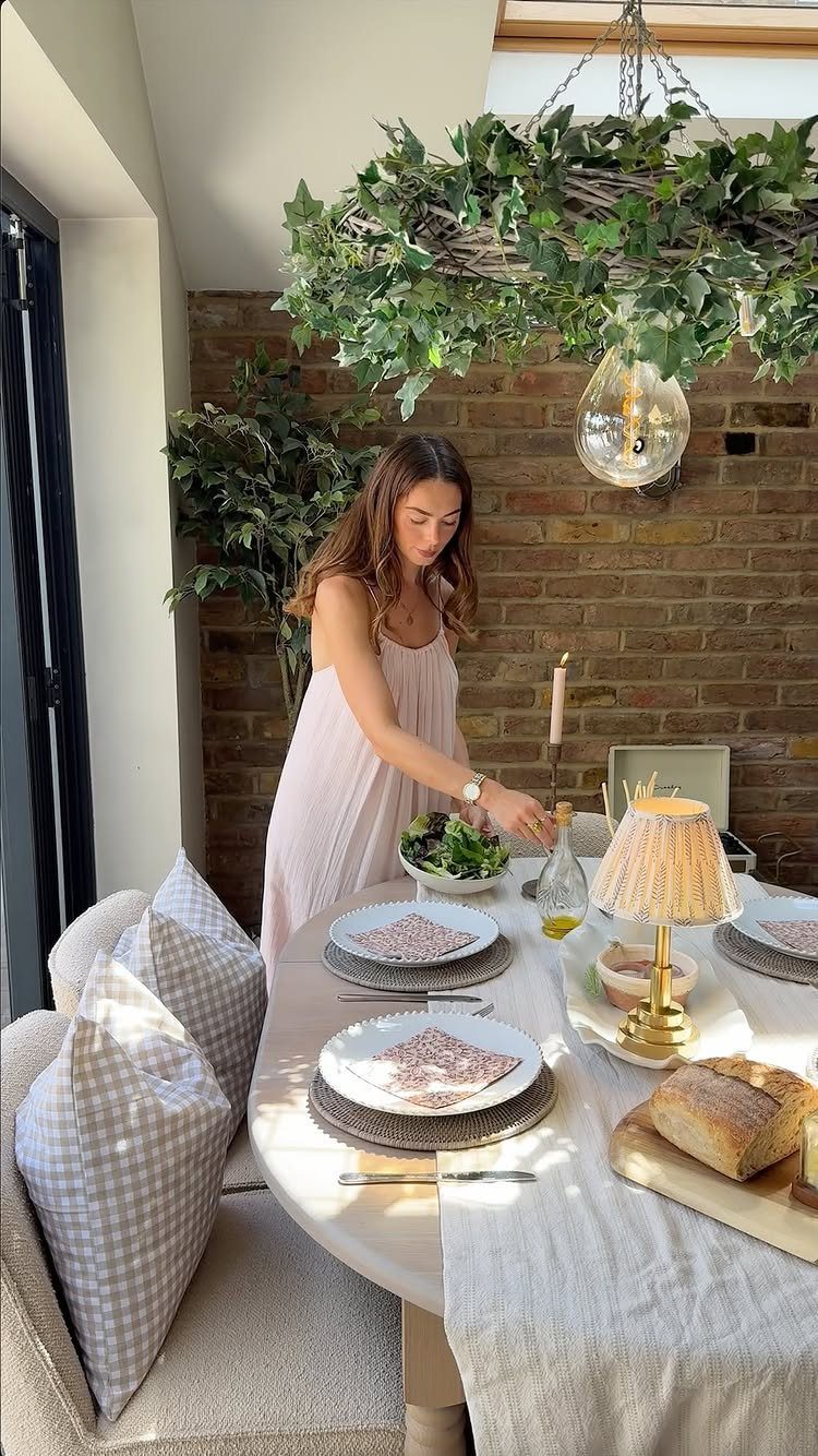 Woman setting a round white table with white stoneware dinnerware and fresh bread.