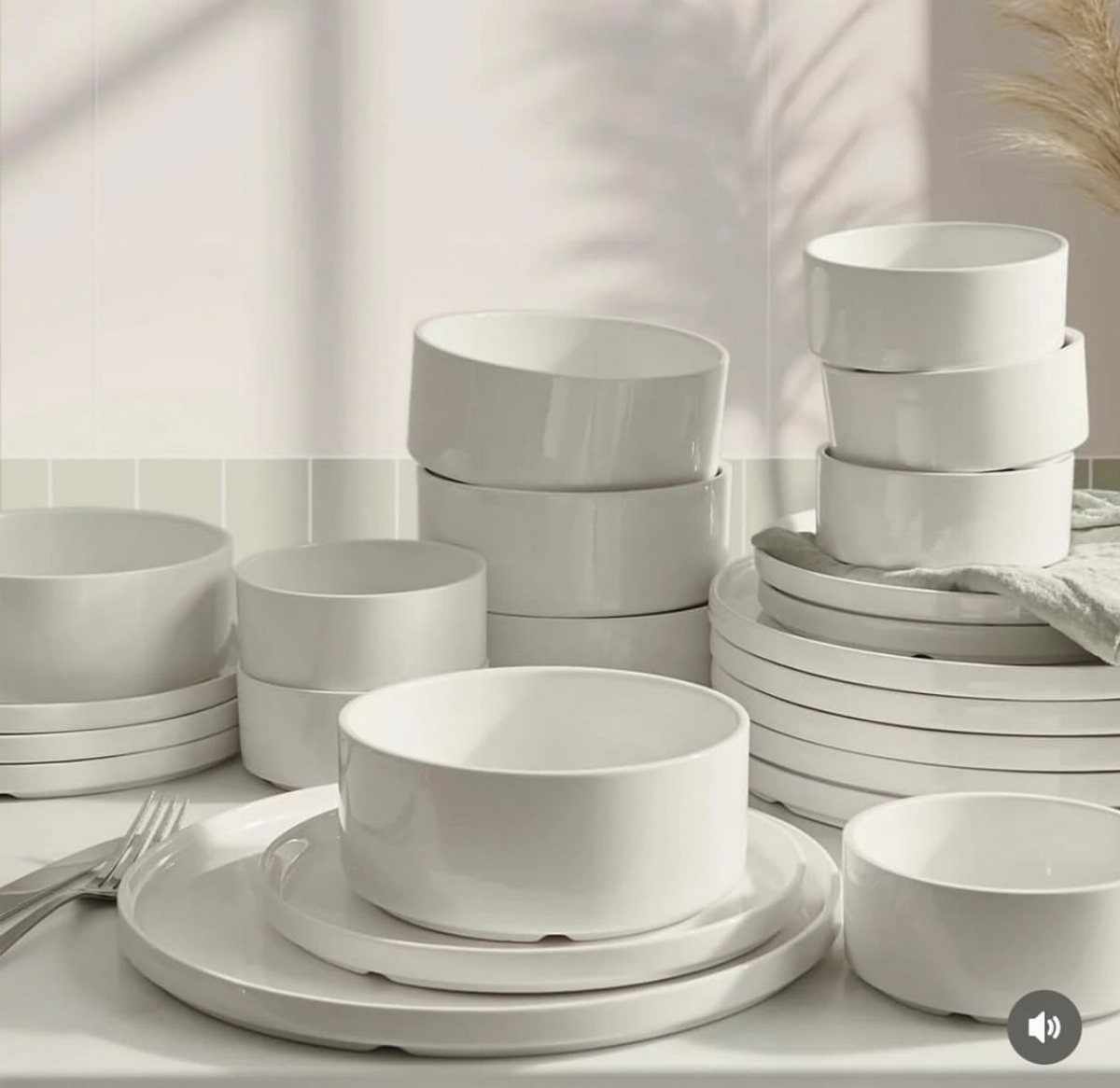 White stoneware bowls and plates stacked on a white surface in bright lighting.