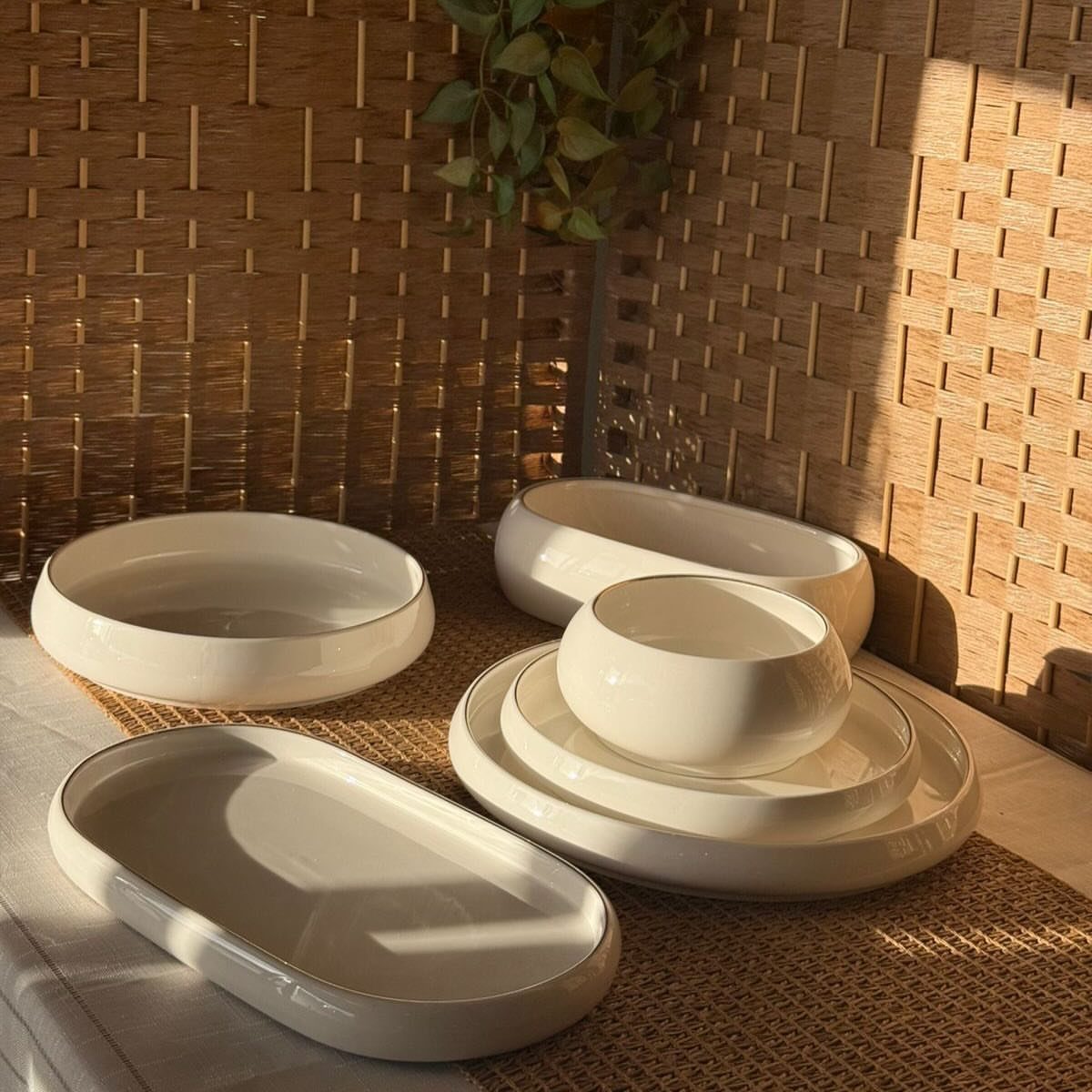 White stoneware dishes including bowls and plates on a woven mat by bamboo.
